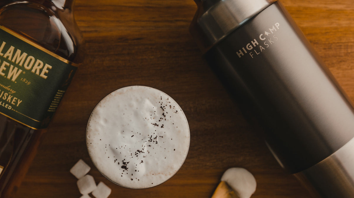 Irish Coffee in a camping tumbler next to a vacuum insulated firelight flask that fits a whole bottle of whiskey, wine and cocktails